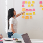 A woman leading a brainstorm session on a whiteboard with post it notes