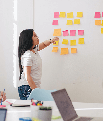 A woman leading a brainstorm session on a whiteboard with post it notes