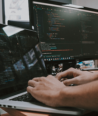 Typing on a laptop screen with a larger desktop screen in the background