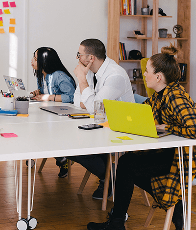 Three people sitting at a conference table with a green colored laptop