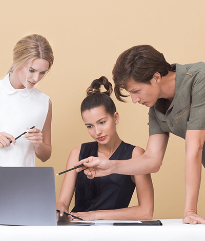 Three people huddled over a laptop while one of them points to something on the screen