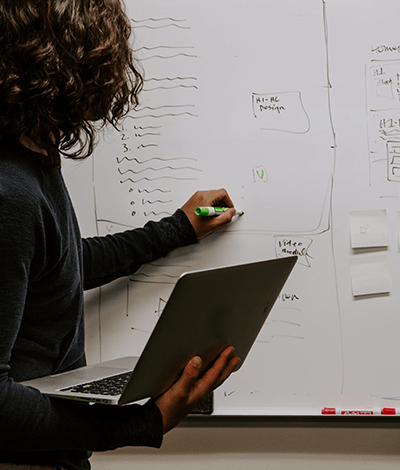 A person is holding their laptop while writing on a whiteboard