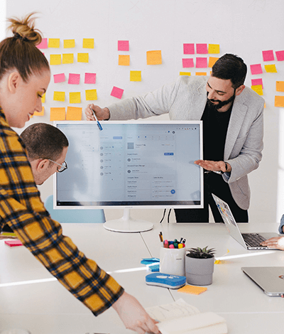 A team brainstorming with post-it notes on a whiteboard, while a team member points to something on the computer screen