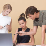 Three people huddled over a laptop while one of them points to something on the screen