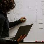 A person is holding their laptop while writing on a whiteboard